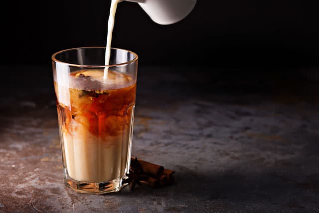 milk being poured into a glass of Indian Chai