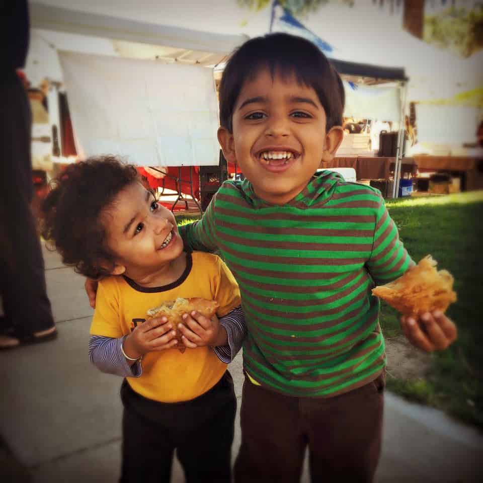two children holding samosas and smiling
