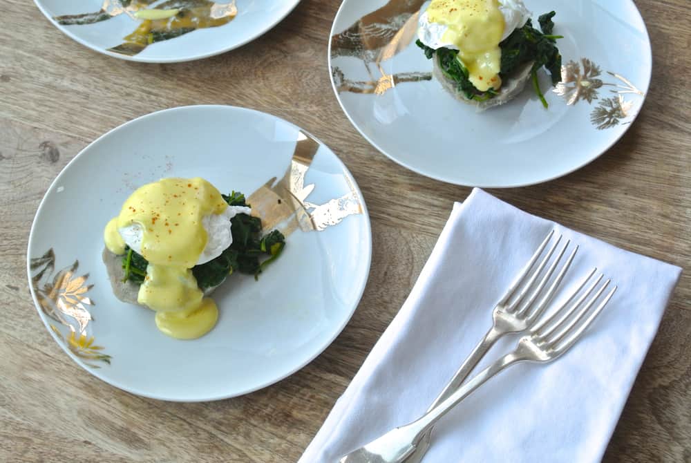 two servings of eggs sardou on white plates with forks