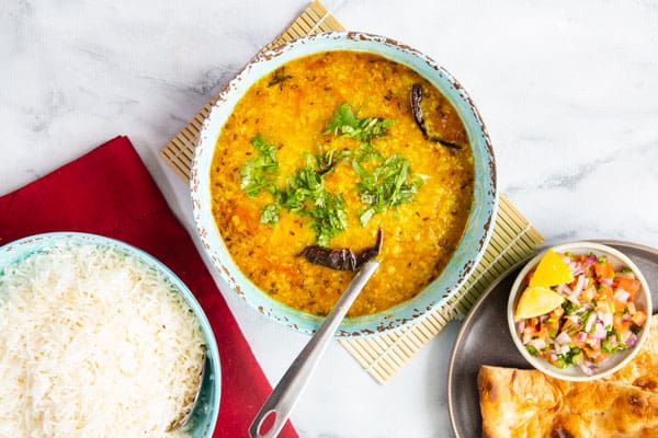A bowl of Dal tadka served with steamed basmati rice, naan and a simple salad.