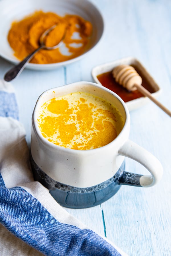 A cup of traditional golden milk in front of a plate of turmeric powder and honey