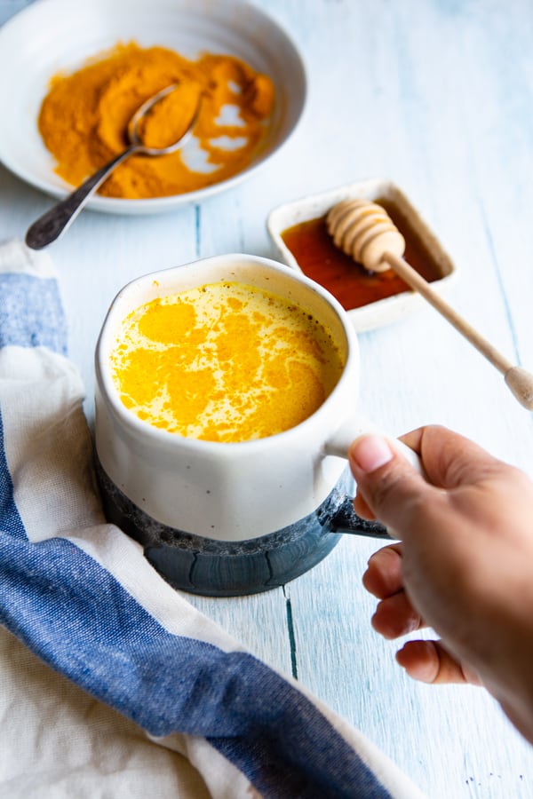 A cup of golden milk, a plate of turmeric powder and honey