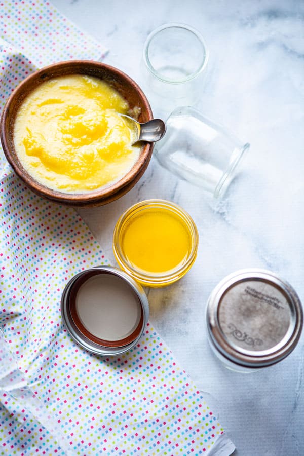 A bowl of ghee with a few ghee filled mason jars around it.