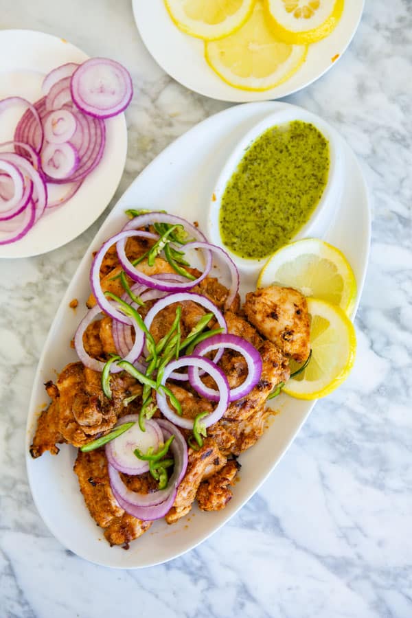 Tandoori Chicken on a platter served with green chutney, red onion rings and sliced chili pepper