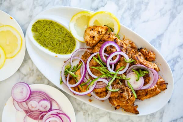 Tandoori Chicken on a platter served with green chutney, red onion rings and sliced chili pepper