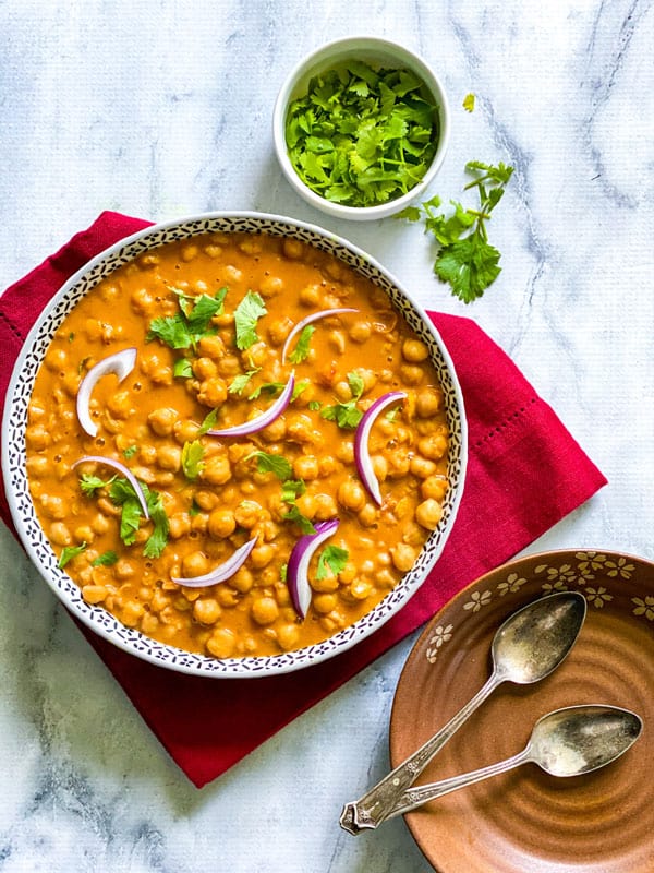 Vegan Tikka Masala Curry in a bowl with cilantro for garnish and two plates to serve the food in