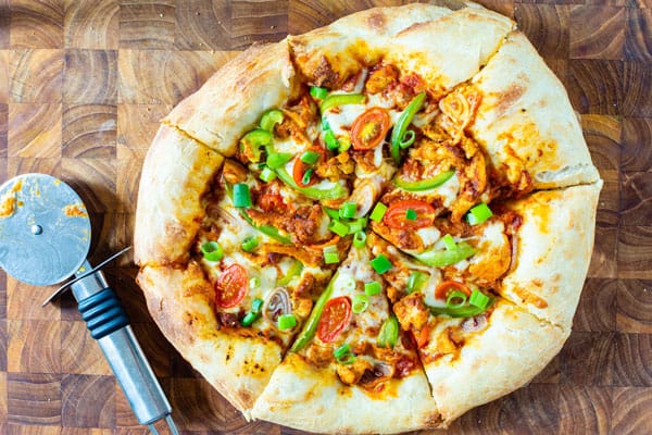Indian Pizza displayed on a chopping board with a pizza cutter by it sside.
