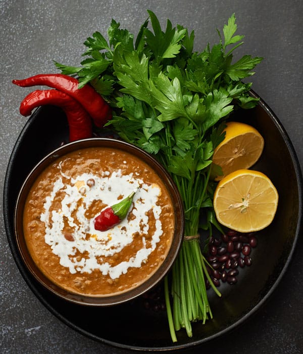 Bowl with Dal Makhni, served on a plate with lemon wedges, chili pepper and cilantro